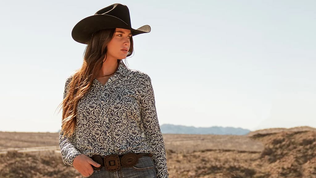 Stetson: A rugged cowboy, dressed in traditional attire including a Stetson hat, strolls alongside a majestic horse amidst the breathtaking mountainous landscape.
