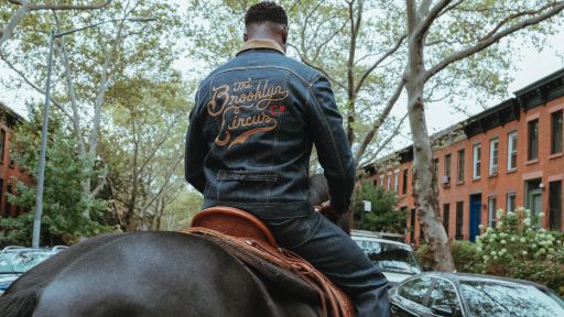 Lee 101: A man dressed in a denim jacket and jeans is riding a horse on a street.