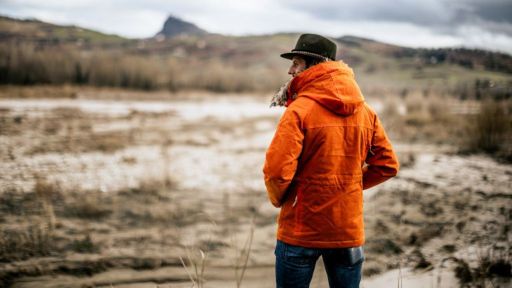 Manifattura Ceccarelli:  A male individual wearing an orange jacket is standing on muddy terrain.